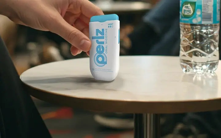 A mint flavoured Perlz dispenser stood upright on a small table with a hand reaching out to pick it up