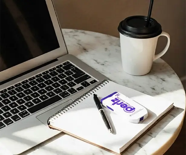 Laptop, notebook, pen, and coffee cup on a marble surface featuring a Perlz dispenser