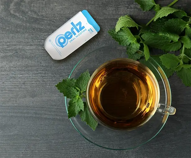 Perlz dispenser next to a cup of tea and mint leaves on a wooden surface